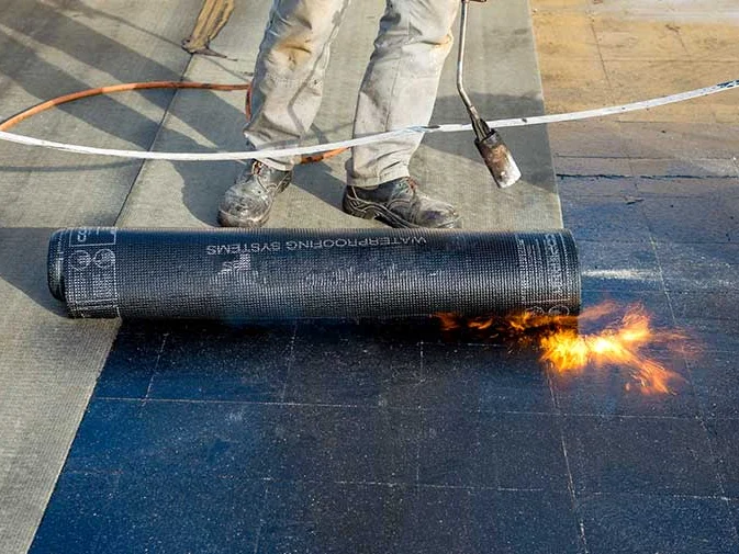 Bitumen dakbedekking wordt uitgerold en gebrand