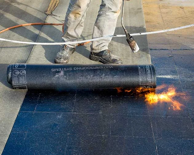 Bitumen dakbedekking wordt uitgerold en gebrand
