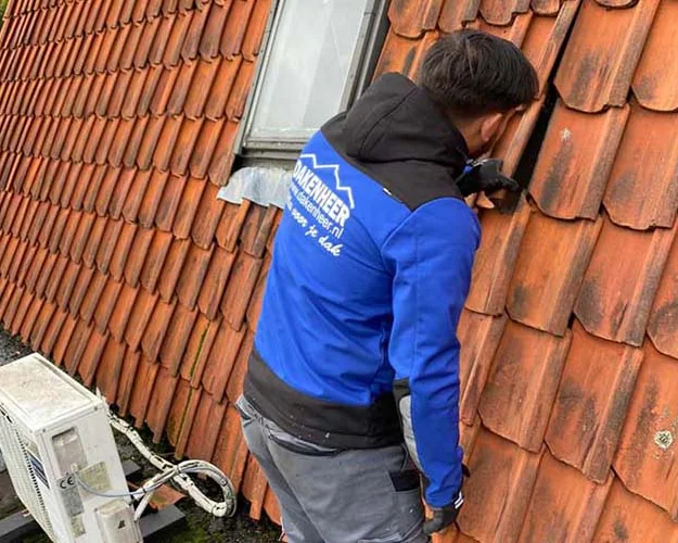 Dakdekker repareert een daklekkage tussen rode dakpannen